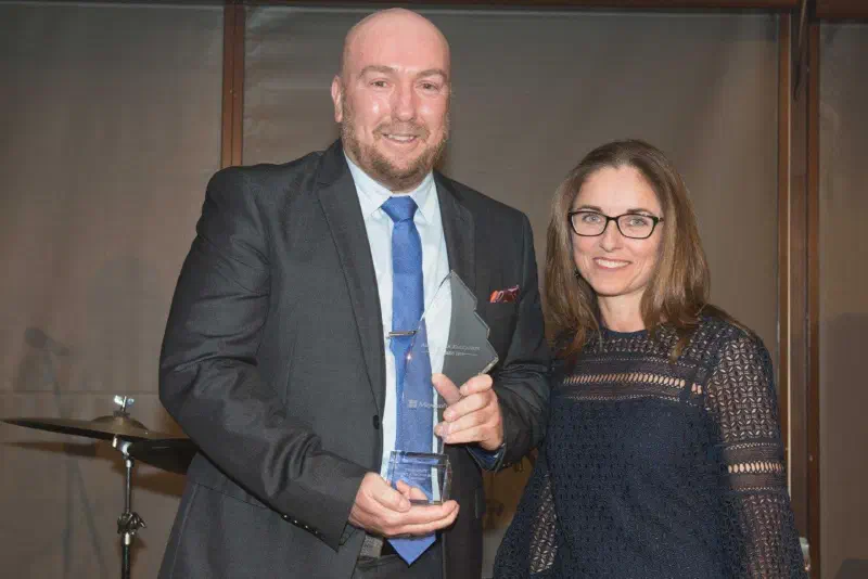 Carolyn and Paul McDermott standing side by side, Paul holding award